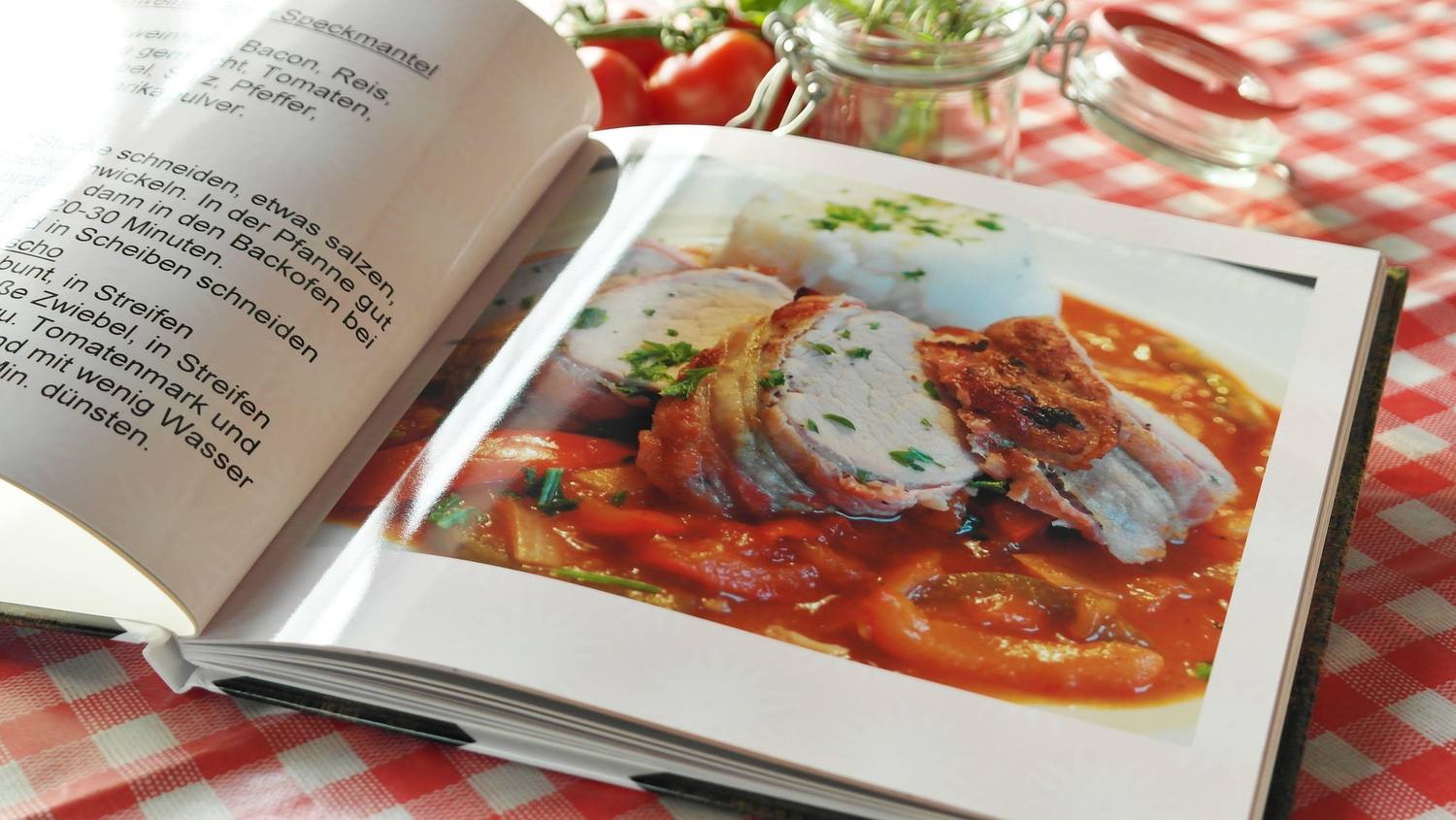 Un livre de cuisine ouvert sur une table, à côté de tomates fraîches